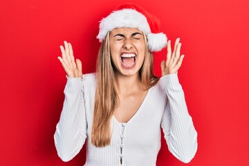 Poster - Beautiful hispanic woman wearing christmas hat celebrating mad and crazy for success with arms raised and closed eyes screaming excited. winner concept