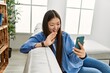 © Krakenimages.com - Young chinese girl having video. call using smartphone sitting on the sofa at home.