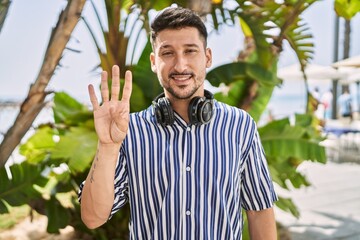 Poster - Young handsome man listening to music using headphones outdoors showing and pointing up with fingers number four while smiling confident and happy.