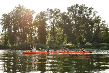 Wall Mural - Canoe with young people boating together on a river surrounded by peaceful summer nature