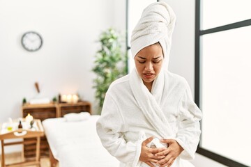 Sticker - Young brunette woman wearing towel and bathrobe standing at beauty center with hand on stomach because indigestion, painful illness feeling unwell. ache concept.