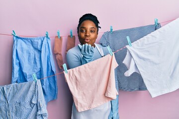 Poster - African american woman with braided hair washing clothes at clothesline looking at the camera blowing a kiss with hand on air being lovely and sexy. love expression.