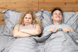 Happy man and disgruntled woman lying in bed under the covers. Relationship concept 
