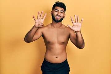 Canvas Print - Arab man with beard wearing swimwear shirtless showing and pointing up with fingers number nine while smiling confident and happy.