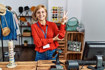 Sticker - Middle age blonde woman working working as manager at retail boutique smiling with happy face winking at the camera doing victory sign. number two.