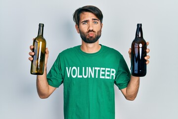 Young hispanic man wearing volunteer t shirt holding recycling bottle glass looking at the camera blowing a kiss being lovely and sexy. love expression.