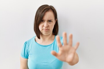 Wall Mural - Young down syndrome woman standing over isolated background doing stop sing with palm of the hand. warning expression with negative and serious gesture on the face.