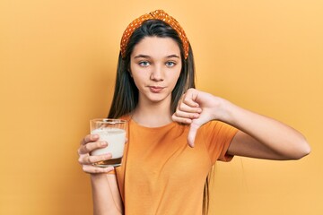 Sticker - Young brunette girl drinking a glass of milk with angry face, negative sign showing dislike with thumbs down, rejection concept