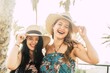 Portrait of two beautiful and cheerful female friends holding straw hats outdoors during summer holiday. Joyful fashionable female tourists with straw hats