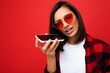 photo of beautiful upset young brunet woman wearing stylish red shirt white t-shirt and red sunglasses isolated over red background using mobile phone recording voice message looking at camera