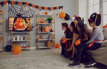 Wall Mural - Kids in spooky costumes of witches, pirates and vampires together watching children's Halloween movie sitting on sofa in interior with festive orange black pumpkin decor at fancy dress party at home