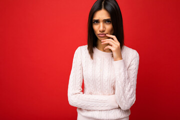 Wall Mural - Portrait of young sad angry dissatisfied cute attractive brunette woman with sincere emotions wearing casual pullover isolated over red background with empty space