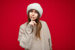 © Ivan Traimak - Photo of young pretty nice dark blonde woman with sincere emotions wearing beige jersey and beige hat isolated over red background with empty space and showing hush gesture with finger. Shhh sign