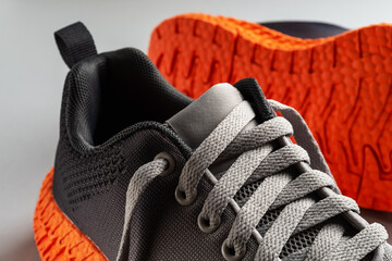Elastic laces of gray mesh fabric sneakers with orange grooved sole close-up. Lacing up the modern textile trainers for sport, fitness and active lifestyle. Pair of new stilysh sport shoes.