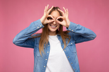 Wall Mural - Photo of young positive happy smiling beautiful woman with sincere emotions wearing stylish clothes isolated over background with copy space and showing glasses gesture with hands