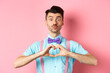 Happy Valentines day. Funny young man waiting for lovers kiss, pucker lips and show heart sign, I love you gesture, express feelings on date, pink background