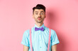 Funny young man waiting for kiss with puckered lips and silly face, standing on romantic pink background. Concept of love and Valentines day