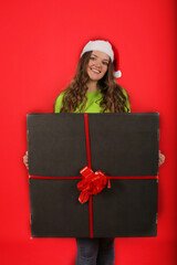 Wall Mural - a young girl in a Santa Claus hat holds a large black gift box in her hands