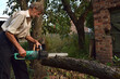 A man cuts off with an electric saw a branch of a broken tree after a storm.