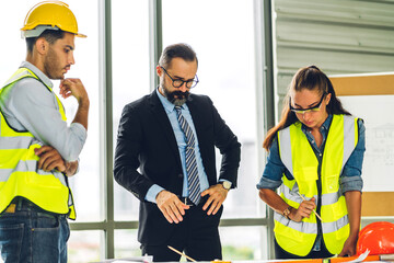 Professional of team architect industrial engineer cargo foreman in helmet working new construction project architectural plan with blueprint and tool on table at building construction site