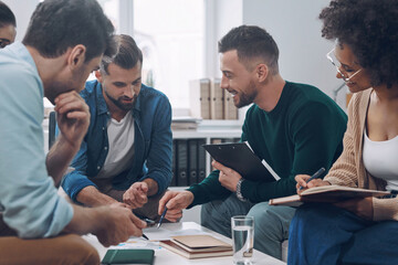 Wall Mural - Group of modern young people discussing business while sitting in the office together