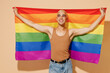 © ViDi Studio - Young activist minded smiling fun blond latin gay man 20s with make up in beige tank shirt hold rainbow flag look aside isolated on plain light ocher background studio People lgbt lifestyle concept.