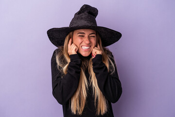 Wall Mural - Young Russian woman disguised as a witch celebrating Halloween isolated on purple background covering ears with hands.
