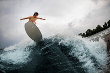 Great View Of Strong Energy Man Skilfully Jumping Over Splashing Wave On Wakesurf Board.