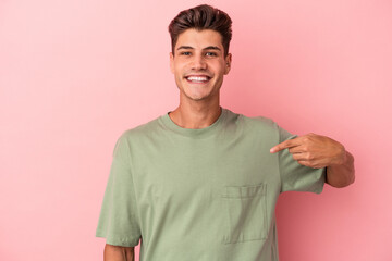 Young caucasian man isolated on pink background person pointing by hand to a shirt copy space, proud and confident