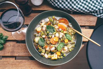 Wall Mural - Top view of delicious minestrone soup in a plate on wooden table and glass of red wine outdoors in the garden