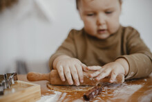 Adorable Baby Girl Kneading Dough With Wooden Rolling Pin For Gingerbread Cookies On Messy Table, Hands Close Up. Cute Toddler Daughter Helps Mother Making Christmas Cookies. Authentic Moments