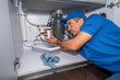 © spatesphoto - Plumber working under a kitchen sink