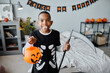 © Seventyfour - Waist up portrait of teenage African-American boy holding Halloween bucket while making faces at camera indoors, copy space