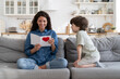 © DimaBerlin - Smiling mom enjoy reading greetings from handmade cute postcard present from small son kid on mother's day, birthday or valentines. Emotional young parent excited getting gift on holiday from child