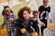 © Seventyfour - Group of smiling African-American kids trick or treating outdoors and walking to camera holding pails