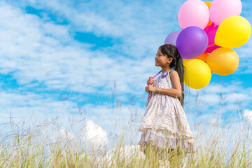 Wall Mural - Cheerful cute girl holding balloons running on green meadow white cloud and blue sky with happiness. Hands holding vibrant air balloons play on birthday party happy times summer on sunlight outdoor