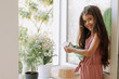 © КРИСТИНА Игумнова - happy kid girl taking care of houseplants at home, dressed in stylish dusty pink outfit. the concept of home gardening. High quality photo