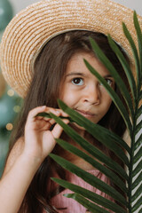 Wall Mural - Face of a little girl surrounded by tropical leaves. Closeup portrait of a beautiful swarthy baby with perfect skin and dark hair. Natural cosmetics, health, cleanliness, skin care, beauty concept