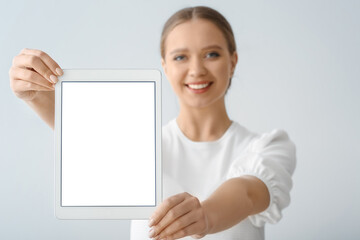 Beautiful young woman holding tablet computer with blank screen on grey background