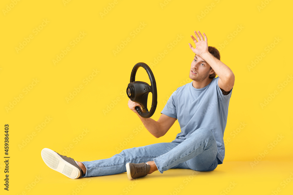 Tired young man with steering wheel on color background