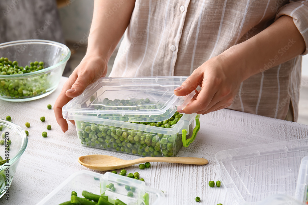 Woman closing plastic container with frozen peas on light background, closeup
