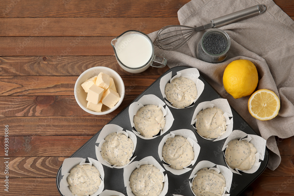 Baking tin with uncooked poppy seed muffins on wooden table