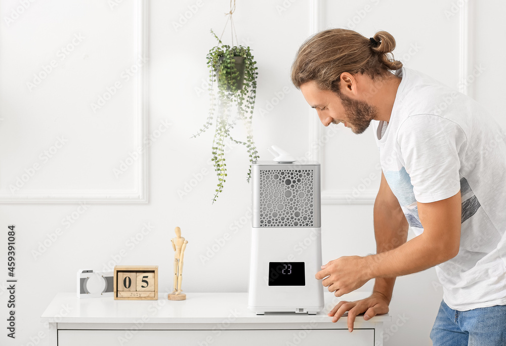 Young man switching on modern humidifier at home