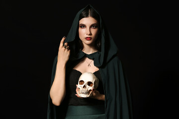 Wall Mural - Young witch with human skull on dark background