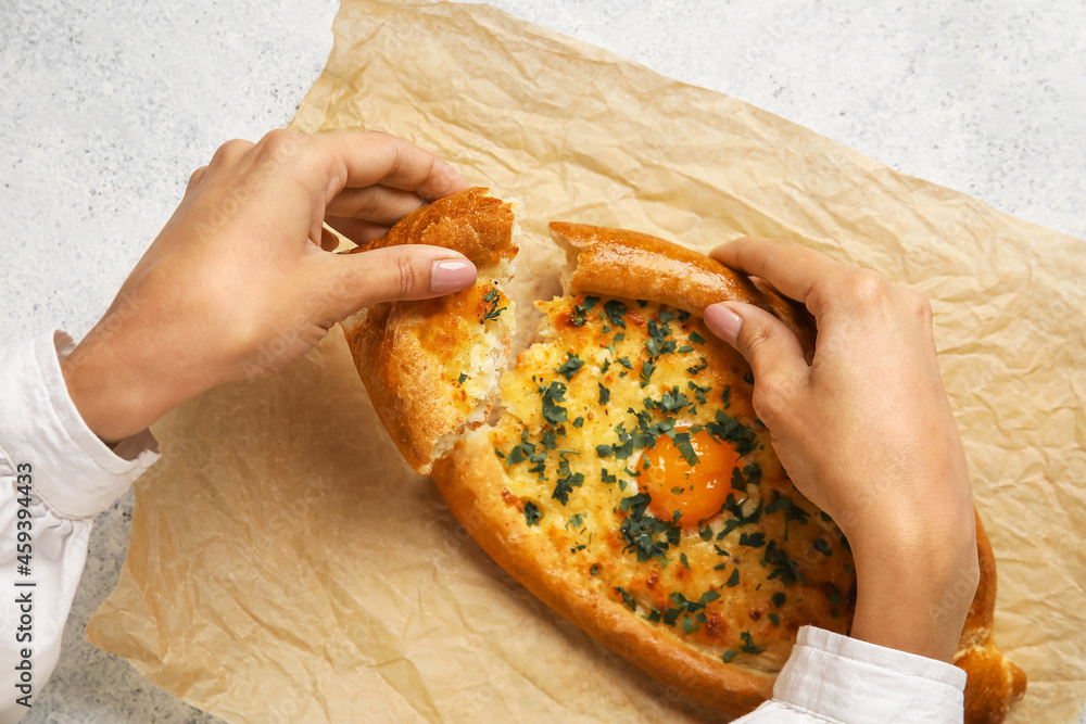 Woman eating tasty Ajarian khachapuri on light background