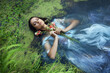 © angel_nt - Art beautiful romantic woman lies in swamp in blue long dress with flowers. Portrait brunette in transparent dress in water swamp mud duckweed. Book cover