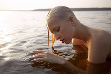 Nude Naked Sexy Woman In Water At Sunset. Beautiful Blonde Woman With Short Wet Hair And Big Breasts, Art Portrait In Sea
