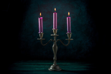 Burning candles in a vintage candle holder on a dark background