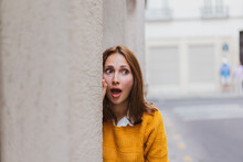 Shocked Young Woman Looking Away While Standing By Wall