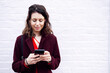 © Westend61 - Smiling woman using smart phone in front of white wall